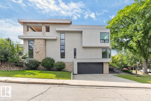 Modern architectural facade with a flat roofline, stucco and stone-clad exterior, a recessed balcony, a two-car garage, and a concrete driveway - 14A Birch Drive, St. Albert, AB 