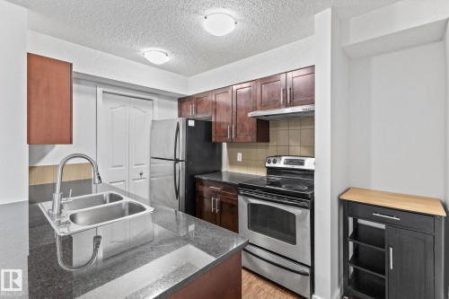 Kitchen featuring dark wood cabinetry, stainless steel appliances, a double basin sink with a high-arc faucet, and dark countertops - #306 530 Watt Bv Sw, Edmonton, AB 