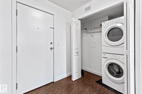 Built-in laundry closet with stacked appliances, white bi-fold doors, and wire shelving - #306 530 Watt Bv Sw, Edmonton, AB 