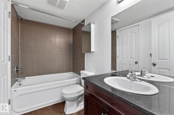 Tub/shower combination with tile surround, wood-finish flooring, dark wood vanity with white oval sink, and large wall-mounted mirror - 