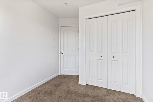 Neutral wall paint, textured carpet, white interior door, and bi-fold closet doors - #306 530 Watt Bv Sw, Edmonton, AB 