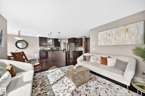 Open-concept living area featuring wood-finish flooring, recessed lighting, and a kitchen with dark cabinetry, stainless steel appliances, and pendant lighting over an island - 12035 168 Avenue Nw, Edmonton, AB 