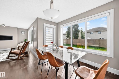 Expansive windows, wood-finish flooring, recessed fireplace, contemporary ceiling light fixture, and a modern dining table - 12035 168 Avenue Nw, Edmonton, AB 