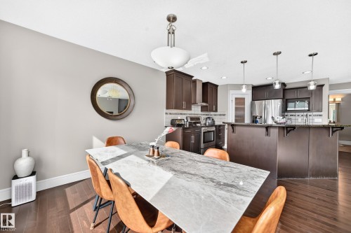Open-concept kitchen and dining area featuring dark wood-finish cabinetry, stainless steel appliances, a breakfast bar, and wood-finish flooring - 12035 168 Avenue Nw, Edmonton, AB 