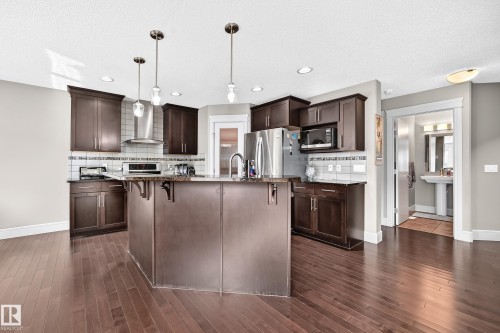 Kitchen featuring dark wood-finish cabinetry, stainless steel appliances, a center island with pendant lighting, and wood-finish flooring - 12035 168 Avenue Nw, Edmonton, AB 