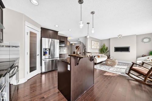 Wood-finish flooring throughout, stainless steel appliances, dark wood cabinetry, recessed lighting, and a modern fireplace - 12035 168 Avenue Nw, Edmonton, AB 