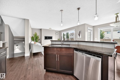 Wood-finish flooring throughout, kitchen island with built-in sink, stainless steel dishwasher, and dark cabinetry - 12035 168 Avenue Nw, Edmonton, AB 