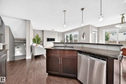 Wood-finish flooring throughout, kitchen island with built-in sink, stainless steel dishwasher, and dark cabinetry - 