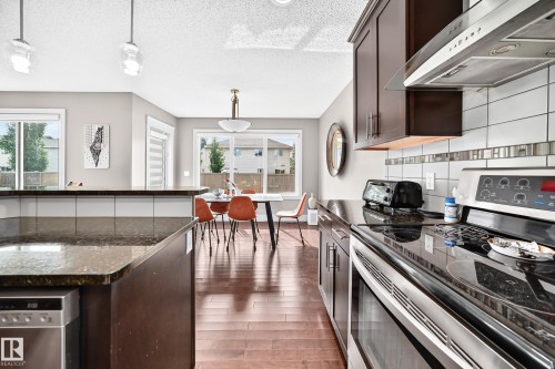 Kitchen featuring dark wood-finish cabinetry, stainless steel appliances, dark countertop, and tile backsplash with decorative accent - 12035 168 Avenue Nw, Edmonton, AB 