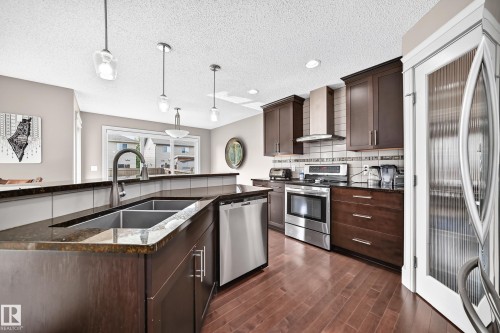 Kitchen with dark wood cabinetry, stainless steel appliances, granite countertops, and wood-finish flooring - 12035 168 Avenue Nw, Edmonton, AB 