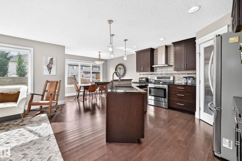 Open-concept kitchen and living area featuring wood-finish flooring, dark wood cabinetry, stainless steel appliances, and recessed lighting - 12035 168 Avenue Nw, Edmonton, AB 