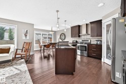Open-concept kitchen and living area featuring wood-finish flooring, dark wood cabinetry, stainless steel appliances, and recessed lighting - 