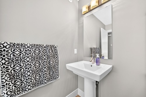Pedestal sink with a polished chrome faucet, rectangular mirror, and a three-light vanity fixture - 12035 168 Avenue Nw, Edmonton, AB 