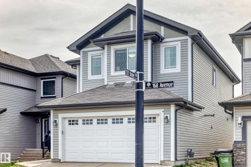 Two-story exterior with light gray siding, white framed windows, an attached garage with a white door, and a black shingled roof - 12035 168 Avenue Nw, Edmonton, AB 