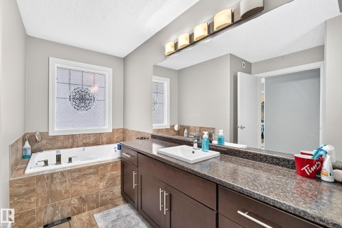 Built-in soaking tub with tile surround, stained wood-finish double vanity, vessel sink, and large wall-mounted mirror with overhead lighting - 12035 168 Avenue Nw, Edmonton, AB 