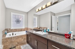 Built-in soaking tub with tile surround, stained wood-finish double vanity, vessel sink, and large wall-mounted mirror with overhead lighting - 