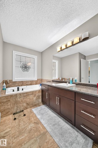 Deep soaking tub with tiled surround, wood-finish vanity with ample storage, integrated sink, and overhead linear vanity lighting - 12035 168 Avenue Nw, Edmonton, AB 