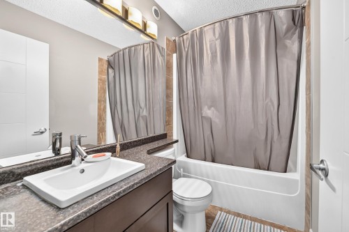 Bathroom featuring a vanity with an integrated rectangular sink, dark granite-style countertop, and a built-in bathtub with shower - 12035 168 Avenue Nw, Edmonton, AB 