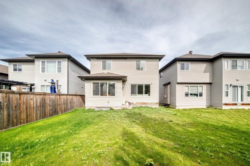 Expansive grassy area bordering a wood-paneled fence, with a two-story residence featuring light-colored siding and a contrasting roof - 12035 168 Avenue Nw, Edmonton, AB 