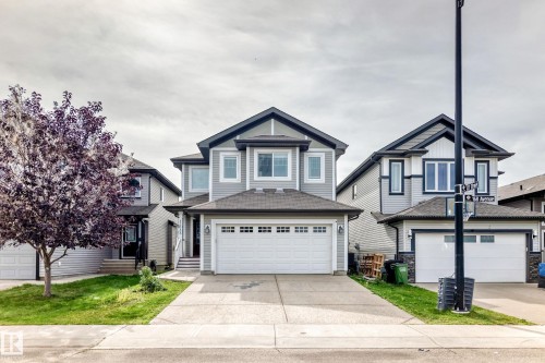 Two-story exterior with light gray siding, dark trim accents, double garage door, concrete driveway, and front lawn - 12035 168 Avenue Nw, Edmonton, AB 