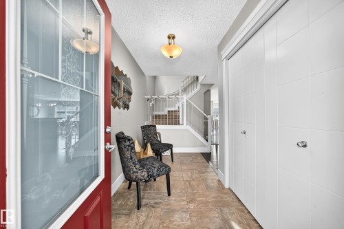Red entry door with decorative glass inserts, tile flooring, built-in closet with panel doors, and a staircase with white railings - 12035 168 Avenue Nw, Edmonton, AB 
