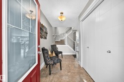 Red entry door with decorative glass inserts, tile flooring, built-in closet with panel doors, and a staircase with white railings - 