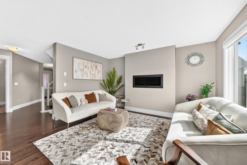 Spacious living area featuring rich wood-finish flooring, a contemporary built-in fireplace, and large windows with natural light - 12035 168 Avenue Nw, Edmonton, AB 