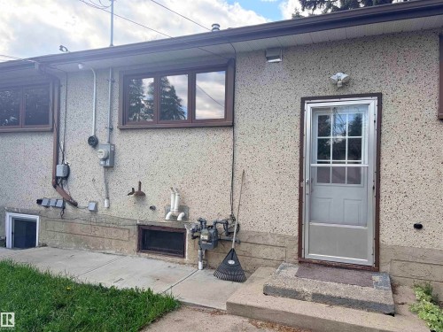 Textured exterior finish with multiple windows, a storm door, and a concrete pathway - 13219 107 Street Nw, Edmonton, AB 
