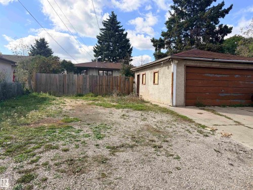 Detached garage with a wood-finish overhead door, stucco exterior, and a gravel driveway - 13219 107 Street Nw, Edmonton, AB 