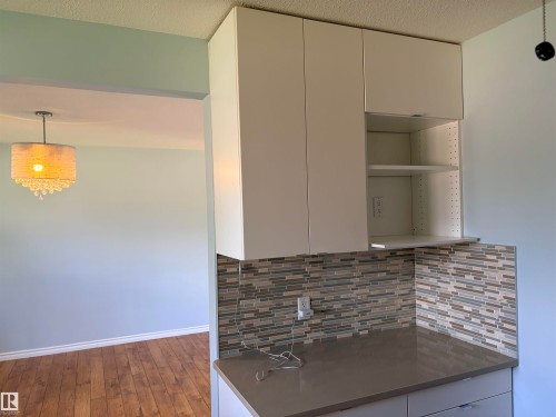 White cabinetry with open shelving, mosaic tile backsplash, solid surface countertop, and wood-finish flooring - 13219 107 Street Nw, Edmonton, AB 