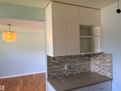 White cabinetry with open shelving, mosaic tile backsplash, solid surface countertop, and wood-finish flooring - 