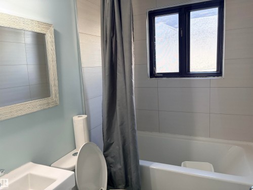 White subway tile surround with a dark-framed window, and a white porcelain tub Upstairs bath - 13219 107 Street Nw, Edmonton, AB 