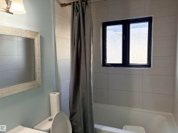 Bathtub with tiled surround, a dark-framed window, and a wall-mounted light fixture Upstairs main bath - 