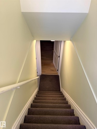 Staircase with carpeted treads, a white handrail, and light-toned wall finishes Leads to basement suite. - 13219 107 Street Nw, Edmonton, AB 