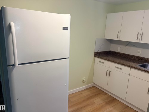 White upper and lower cabinetry with brushed nickel hardware, speckled countertops with a partial backsplash, and wood-finish flooring Basement kitchen - 13219 107 Street Nw, Edmonton, AB 