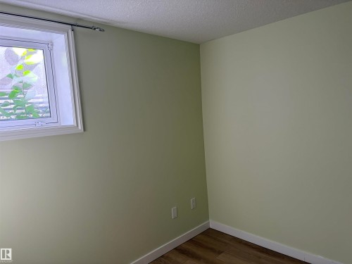 White-trimmed window with privacy glass, light green painted walls, and wood-finish flooring Basement - 13219 107 Street Nw, Edmonton, AB 