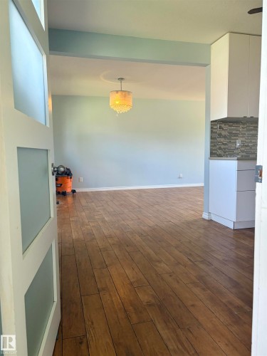 Wood-finish flooring throughout, frosted glass paneled doors, contemporary chandelier, white cabinetry, and a mosaic tile backsplash - 13219 107 Street Nw, Edmonton, AB 