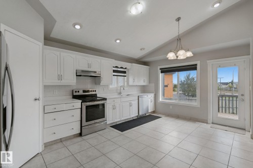 Kitchen featuring white cabinetry, stainless steel appliances, tiled flooring, and a glass-paneled door - 16807 78 Street Nw, Edmonton, AB 