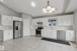 White shaker-style cabinetry, stainless steel appliances, tile flooring, recessed lighting, and a decorative chandelier - 