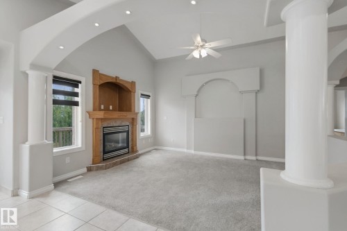 Vaulted ceiling with recessed lighting, central ceiling fan, wood-mantled fireplace with tile surround, large windows with shades, and decorative interior columns - 16807 78 Street Nw, Edmonton, AB 