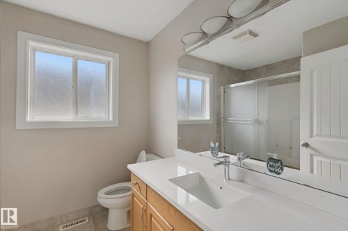 Bathroom featuring a wide vanity with an integrated rectangular sink, wood-finish cabinetry, a large mirror, and a shower with sliding glass doors - 16807 78 Street Nw, Edmonton, AB 