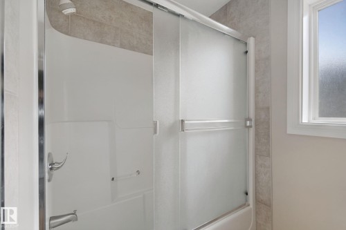 Tub/shower combination with chrome fixtures, sliding frosted glass doors, and tiled surround - 16807 78 Street Nw, Edmonton, AB 