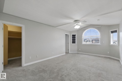 Spacious room featuring vaulted ceilings, a ceiling fan, a large arched window, additional windows with blinds, and carpeted flooring - 16807 78 Street Nw, Edmonton, AB 