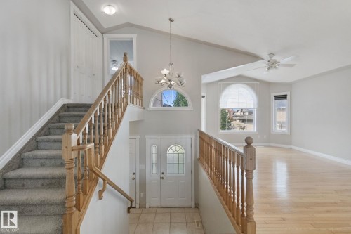 Vaulted ceiling with an attached ceiling fan, large arched window, double entry doors with decorative glass panels, wood-finish flooring, and carpeted stairs with a wood balustrade - 16807 78 Street Nw, Edmonton, AB 