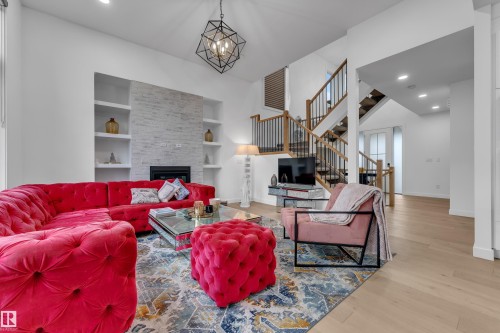 Spacious living area featuring a stone-clad fireplace with built-in shelving, high ceilings, recessed lighting, a modern geometric chandelier, and wood-finish flooring - 1409 Graydon Hill Way Sw, Edmonton, AB 