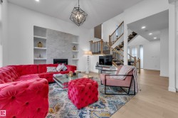 Spacious living area featuring a stone-clad fireplace with built-in shelving, high ceilings, recessed lighting, a modern geometric chandelier, and wood-finish flooring - 