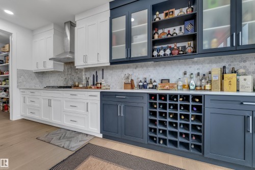 Kitchen featuring dual-tone cabinetry, a tile backsplash, light countertops, and wood-finish flooring - 1409 Graydon Hill Way Sw, Edmonton, AB 