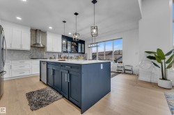 Modern kitchen featuring a large central island with seating, stainless steel appliances, two-tone cabinetry, and wood-finish flooring - 