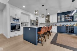 Modern kitchen featuring light wood-finish flooring, white cabinetry, a built-in oven and microwave, a large central island with a contrasting base, and a dedicated beverage station with blue cabinetry and a wine rack - 