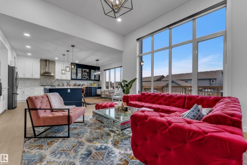 Expansive great room featuring soaring ceilings, a full wall of windows, recessed lighting, wood-finish flooring, and a kitchen with an island, pendant lighting, and built-in cabinetry - 1409 Graydon Hill Way Sw, Edmonton, AB 